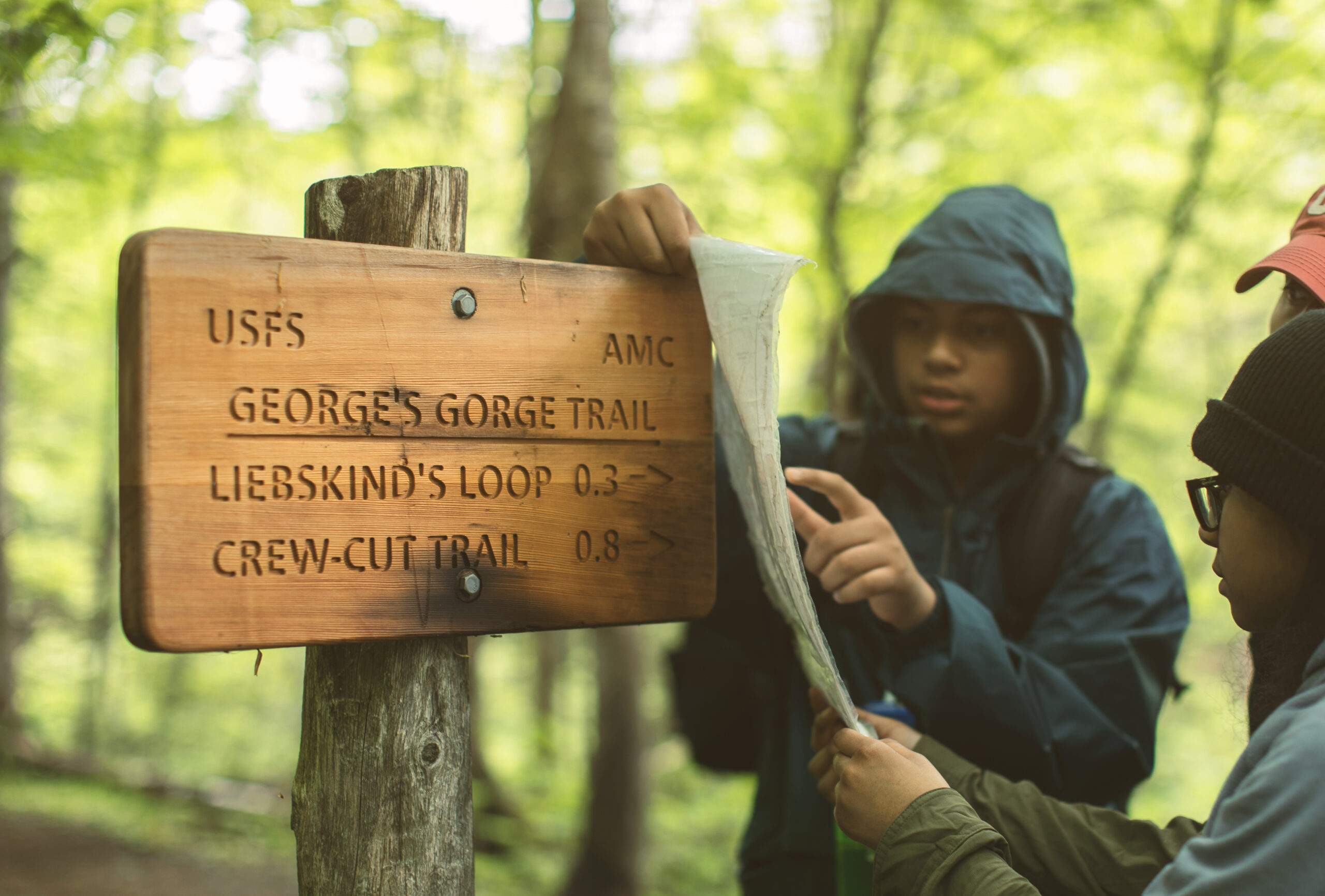 AMC trail sign and three people looking at a map.